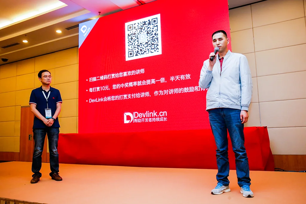 杨永全站在台上，手持话筒讲话，鸟哥站在旁边