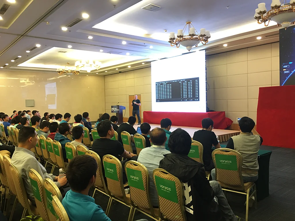 Rasmus 站在台上演讲，台下坐满听众的背影