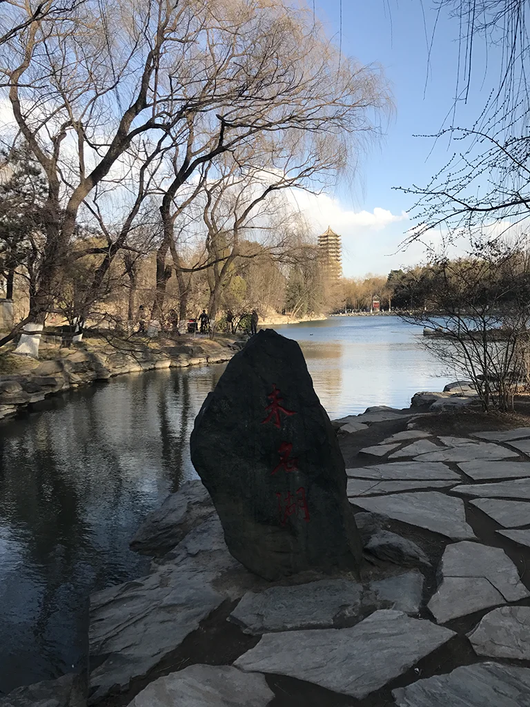 秦灵石立于未名湖岸，红色刻字，远处博雅塔倒映湖面